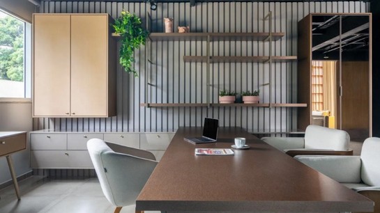 Já neste projeto da Criare Florianópolis, o painel ripado em tom de cinza com armários, prateleiras e gavetões contrasta com a ampla mesa de madeira. Fotos Roberta Gewher